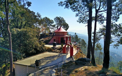 Small temple on a hill crest surrounded by tall pine trees overlooking a valley